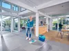 A woman is mopping the floor in a modern, open-plan living space with large windows. Anteprima dell’immagine prodotto