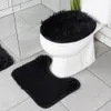 A black fluffy toilet seat cover and a matching toilet mat are shown in a bathroom. Produktbild-Vorschau