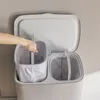 A person's hand is shown placing a fabric liner into one of two compartments of a laundry hamper. Produktbild-Vorschau