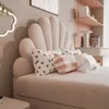 A close-up view of a bed with a shell-shaped headboard and decorative pillows. Produktbild-Vorschau