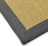 A close-up view of the corner of a sisal rug with a graphite border. Voir les images du produit
