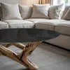 A close-up of a coffee table with a glass top and a wooden base, placed in front of a sofa in a living room. Podgląd zdjęcia produktu