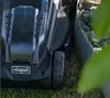 A close-up of a black robotic lawnmower next to a metal border filled with rocks. Náhled obrázku produktu