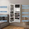 A white jewelry cabinet with its doors open, displaying various compartments for jewelry and makeup, mounted on a wall next to a bed. Náhľad obrázku produktu