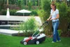 A woman is mowing the lawn in a garden with a swimming pool and umbrella in the background. Produktbild-Vorschau