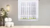 A white sheer curtain with lace trim hangs in a window, with a modern chair and a plant in the foreground. Produktbild-Vorschau