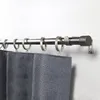 A close-up view of a metal curtain rod with rings and dark gray curtains hanging from it, mounted on a white wall. Produktbild-Vorschau