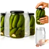 Several jars of pickles are arranged in the foreground, with a hand holding one jar in the upper right corner and an empty jar in the lower right corner. Produktbild-Vorschau