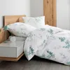 A neatly made bed with white bedding featuring a green floral pattern, next to a wooden headboard and a white nightstand with a small lamp. Produktbild-Vorschau