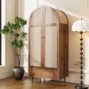A wooden wardrobe with woven doors and a drawer, placed in a room with a plant and a floor lamp. Anteprima dell’immagine prodotto