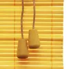 Close-up of two wooden pull cords with decorative ends hanging against a yellow bamboo blind. Produktbild-Vorschau