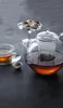 A glass teapot filled with tea, a teacup, and chocolates on a dark surface. Produktbild-Vorschau