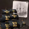 A close-up of a model ship with black sails featuring gold emblems, next to a sketch of a historical sailing ship. Náhled obrázku produktu