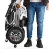 A person stands next to a folded electric wheelchair. Náhľad obrázku produktu