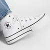 A close-up shot of a white Converse Chuck Taylor All Star high-top sneaker with black accents. Voir les images du produit