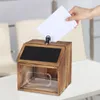 A hand is placing a white paper into a wooden suggestion box with a chalkboard top. Náhled obrázku produktu