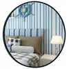 A bedroom scene with a bed, pillows, a lamp, and a clock on the wall, all reflected in a round mirror. Produktbild-Vorschau