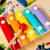 A close-up view of a colorful wooden xylophone with a mallet resting on it, set against a wooden background. Decorative elements like a zebra and water splashes are visible. Podgląd zdjęcia produktu