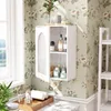 A bathroom cabinet filled with toiletries, placed on a wall with floral wallpaper, next to a window. Produktbild-Vorschau