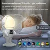 A young person sleeping in bed next to an astronaut-shaped wake-up light alarm clock. Produktbild-Vorschau