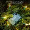 A string of LED lights with a green battery box is draped over lush green foliage, with water droplets on the leaves and battery box, suggesting outdoor use. Produktbild-Vorschau