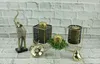 A collection of decorative items including an elephant figurine, a golden apple, and candle holders with candles, arranged on a white brick surface. Produktbild-Vorschau