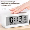 A hand is touching the top of a digital alarm clock, which is displaying the time, date, temperature, and humidity. Produktbild-Vorschau