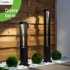 Two black bollard lights are shown in front of a wooden slatted wall, with manicured bushes and white stones in the foreground. Anteprima dell’immagine prodotto