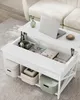 A white coffee table with its lift-top open, revealing storage compartments. A laptop, headphones, books, and other items are neatly organized inside. The table is placed in a living room setting, next to a couch. Náhled obrázku produktu