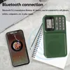 A green DAB radio and a smartphone are placed on a desk next to a laptop and a notebook. Produktbild-Vorschau