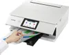 A hand is shown inserting a document into a white Canon PIXMA TS8751 WLAN color multifunction photo printer. Podgląd zdjęcia produktu
