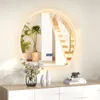 A round LED mirror is mounted on a wall above a dresser with decorative items. Produktbild-Vorschau