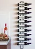 A black metal wine rack mounted on a white wall, holding ten bottles of wine. A bottle of rose wine and a bowl of corks are on a countertop to the left. Náhled obrázku produktu