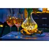 Two glasses of amber-colored drinks with lemon twists and rosemary sprigs sit on a wooden table next to a glass vase filled with water and illuminated by warm white LED micro lights. The vase rests on a piece of driftwood. The scene is set outdoors at dusk Produktbild-Vorschau