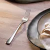 A fork is placed on a wooden table next to a plate with a napkin. Produktbild-Vorschau