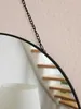A close-up shot of a round mirror hanging from a black chain against a light pink wall. A staircase is visible in the reflection. Produktbild-Vorschau