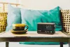 A digital radio and a cup of coffee sit on a wooden table. Voir les images du produit