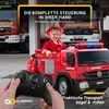 A child dressed as a firefighter is sitting in a red toy fire truck, holding a remote control. Two real fire trucks are in the background. Produktbild-Vorschau