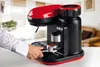 A person's hand is placing a portafilter into a red and black espresso machine with a built-in grinder. Produktbild-Vorschau