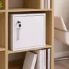 A white safe with a key is placed on a shelf in a wooden bookcase. Books are visible on the shelf below. Produktbild-Vorschau