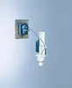 A close-up shot of a toilet cistern fill valve and flush actuator mechanism against a plain blue and gray background. Anteprima dell’immagine prodotto