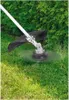 A string trimmer is cutting grass in front of a hedge. Produktbild-Vorschau