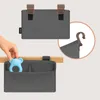 A hand is placing a blue teether into a gray organizer that is attached to a wooden surface. Produktbild-Vorschau