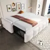 A white sofa bed is shown in a room with framed pictures on the wall and a window in the background. Produktbild-Vorschau