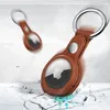 Two brown leather AirTag holders with keyrings are shown, one in the foreground and one blurred in the background, on a cracked concrete surface. Produktbild-Vorschau