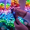 Hands holding a black device with a blue light, in front of a bokeh background of colorful Christmas lights. Náhled obrázku produktu