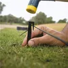 A hand is holding a black plastic stake in the grass while a hammer is about to strike it. Voir les images du produit