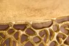 A close-up view of the intricate, golden, filigree design of a table's edge. Produktbild-Vorschau