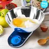 A digital kitchen scale with a stainless steel bowl containing flour and an egg, along with apples and a wooden spoon. Produktbild-Vorschau