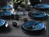 A table setting with blue ceramic plates, wine glasses, and cutlery, arranged on a gray tablecloth. Náhľad obrázku produktu